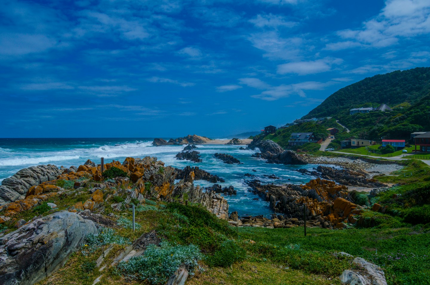 Ocean waves crash against rocky cliffs near a coastal hillside.
