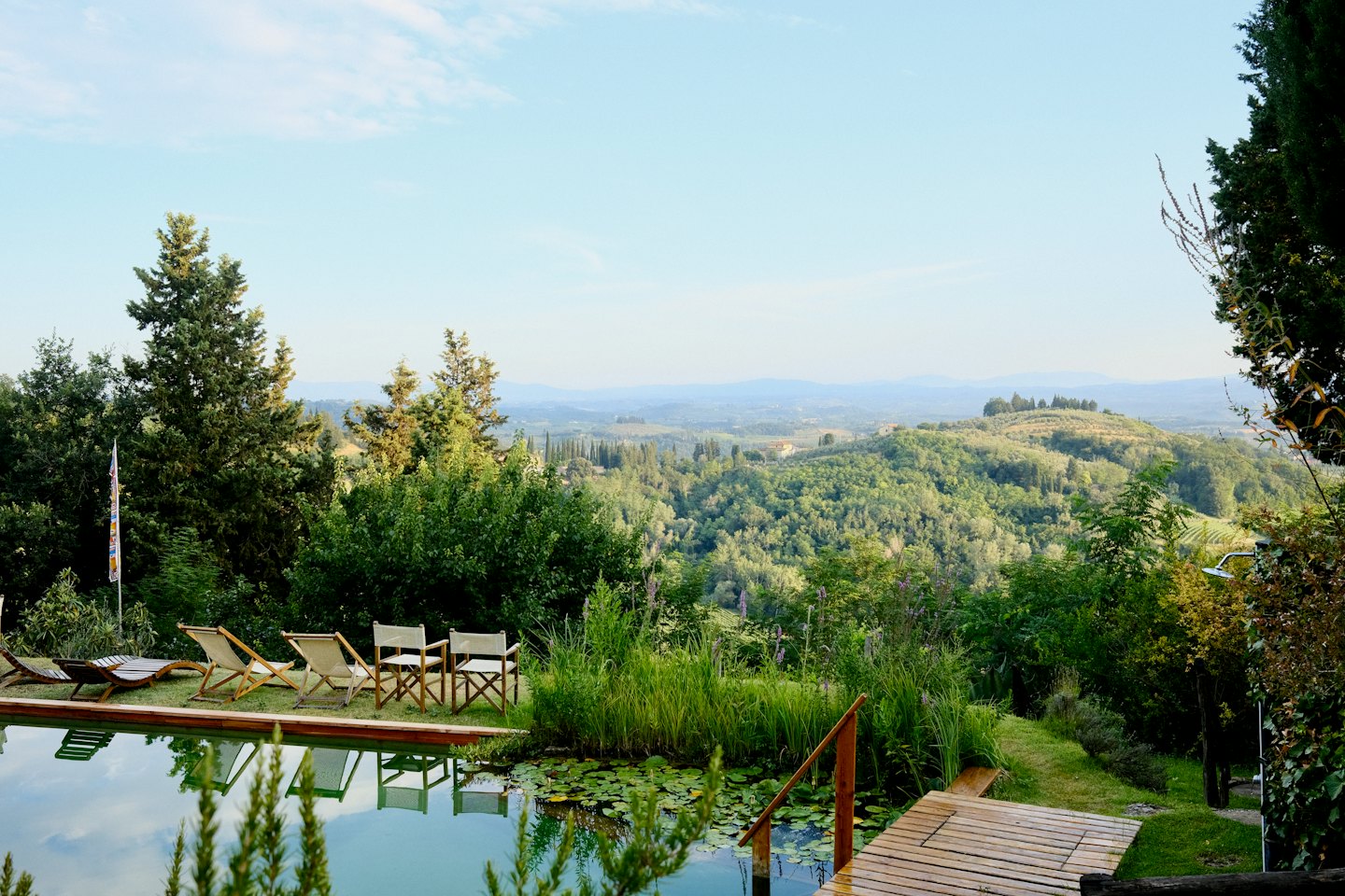 Natural swimming pool with wooden deck overlooking hilly landscape.